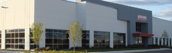 Modern white commercial building with large windows and a small tree outside.