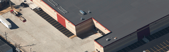 Aerial view of a brick building with a gray roof and industrial surroundings.