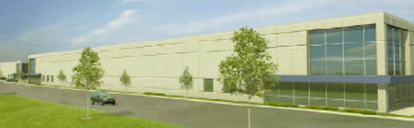 A large beige industrial building with a few small trees and grass in front.