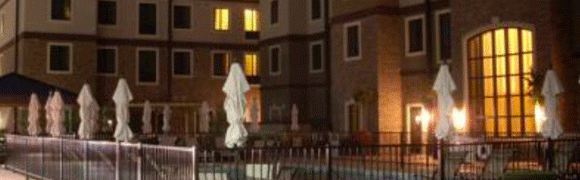 A white umbrella stands closed near a pool at night in a residential area.