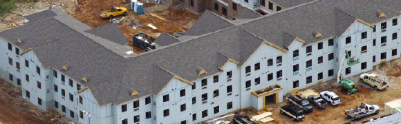A large building under construction with a gray shingled roof.