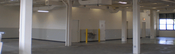 Empty industrial space with a water fountain and yellow safety bollards.